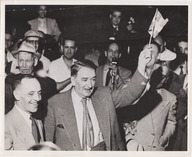 Maurice Duplessis tenant un drapeau du Québec entouré d'une foule de partisans célébrant sa victoire électorale