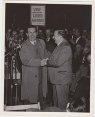 Maurice Duplessis serrant la main de Maurice Bellemare. Ils sont entourés d'une foule de partisans. L'un d'entre eux tient une pancarte sur laquelle il est écrit «Vive l'Union Nationale» 