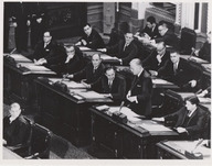 Jean Lesage debout pendant une séance à l'Assemblée nationale. Ses collègues frappent leur bureau de la main. Il est entouré de Pierre Laporte et Paul Gérin-Lajoie.