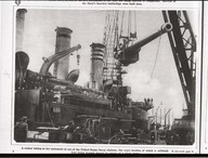 A cruiser taking her armament at one of the United States naval stations, the exact location of which is withheld. A six-inch gun is here being hoisted aboard by means of a giant crane.
