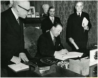 His Excellency Viscount Alexander of Tunis, Governor General of Canada (seated) signs bill relating to terms of union with Newfoundland, while Prime Minister Louis St. Laurent (left), Dr. Gaspard Fauteux (background), speaker of the House and Senator J.H. King (right), speaker of the Senate, look on.
